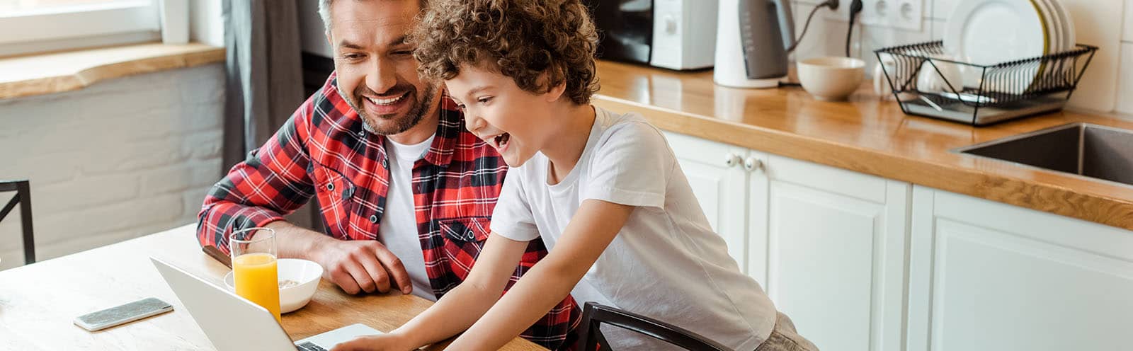 Man and boy having fun with computer at breakfast