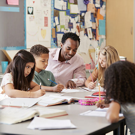 Male teacher works with elementary school kids at their desk